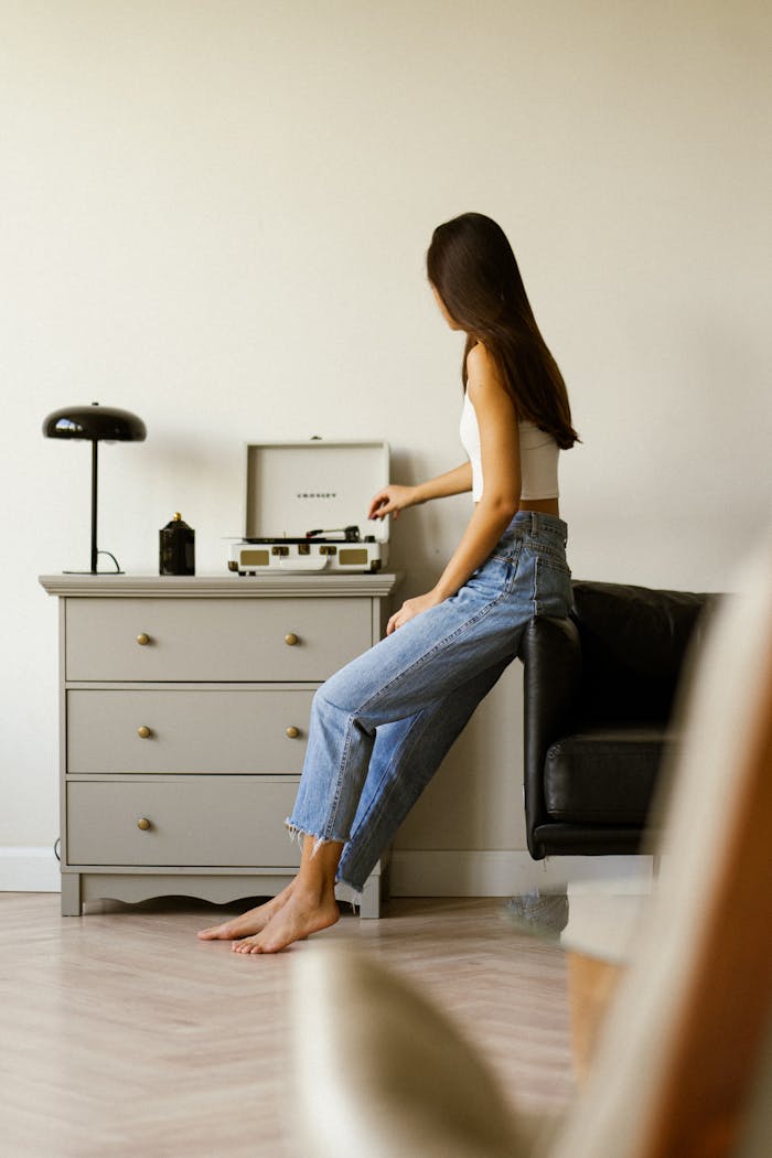 gallery-4 Woman in casual attire enjoying music from a vintage record player in a minimalist living room.