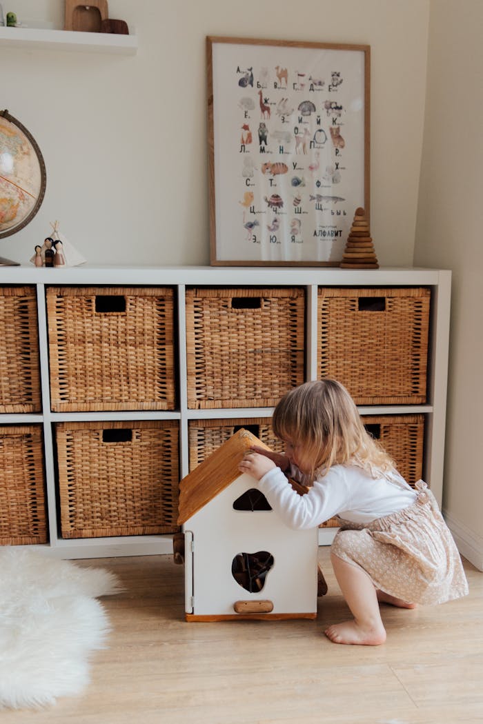 gallery-5 A cute toddler plays with a dollhouse in a cozy room with wooden storage baskets.