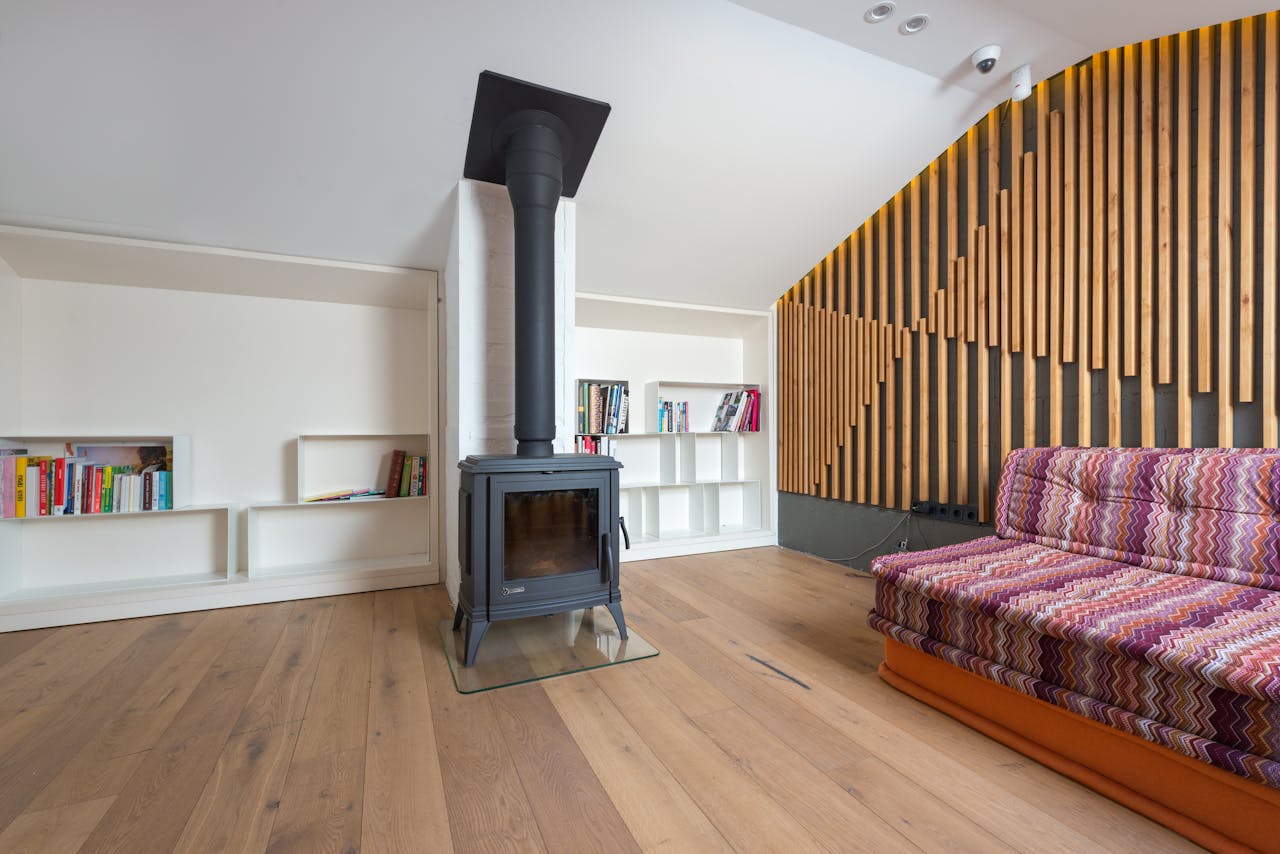 gallery-1 Comfortable sofa placed near wall decorated with wooden planks and fireplace against shelves with books